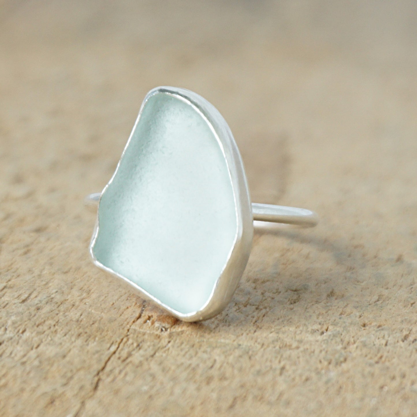 light aqua blue sea glass ring with a sterling silver setting, against a wooden background