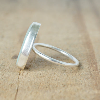 side view of a light aqua blue sea glass ring with a sterling silver setting, against a wooden background