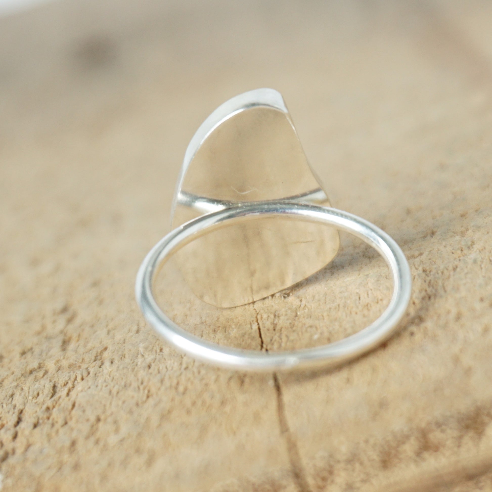 back view of a light aqua blue sea glass ring with a sterling silver setting, against a wooden background