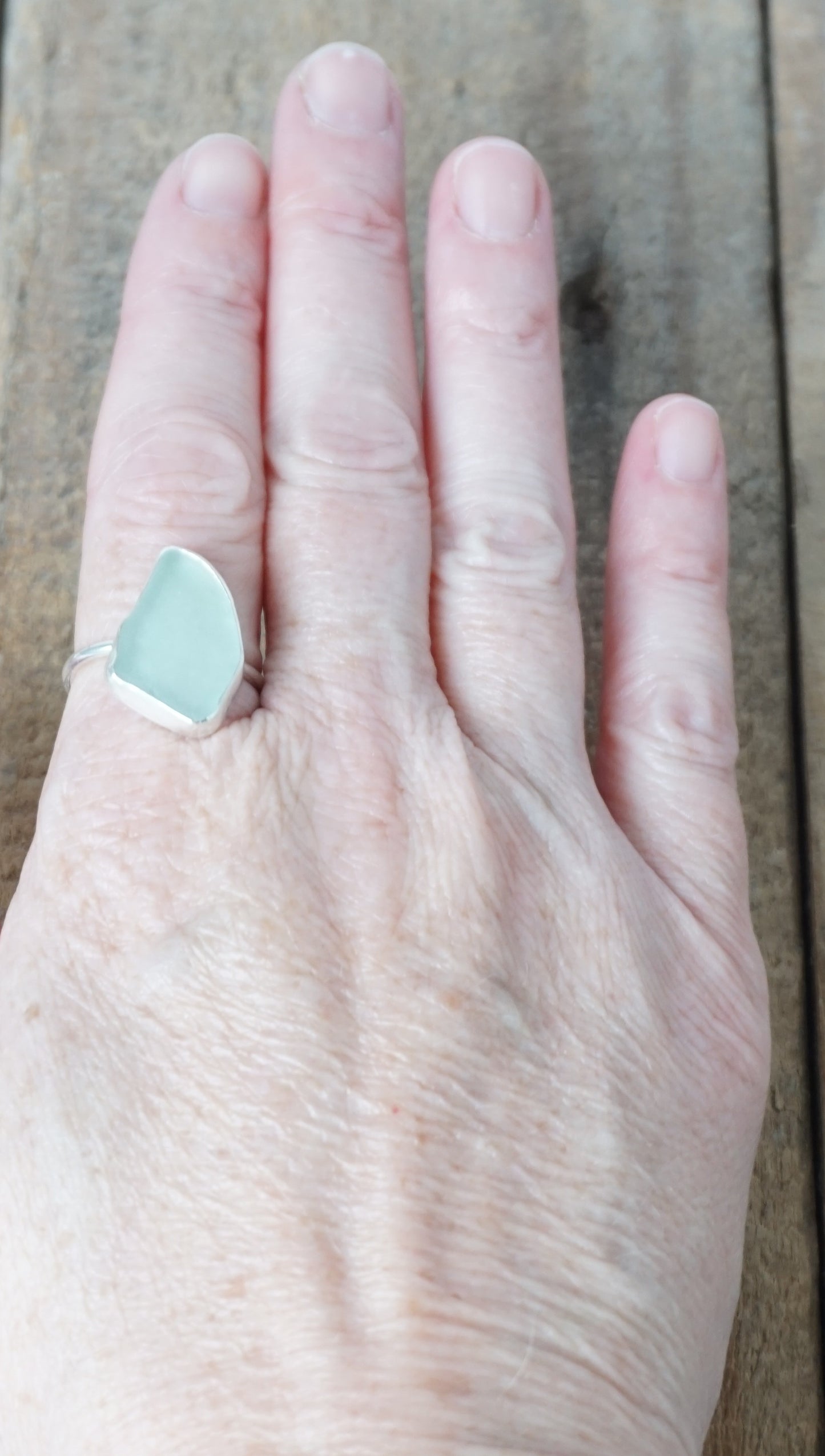 hand wearing a light aqua blue sea glass ring with a sterling silver setting, against a wooden background