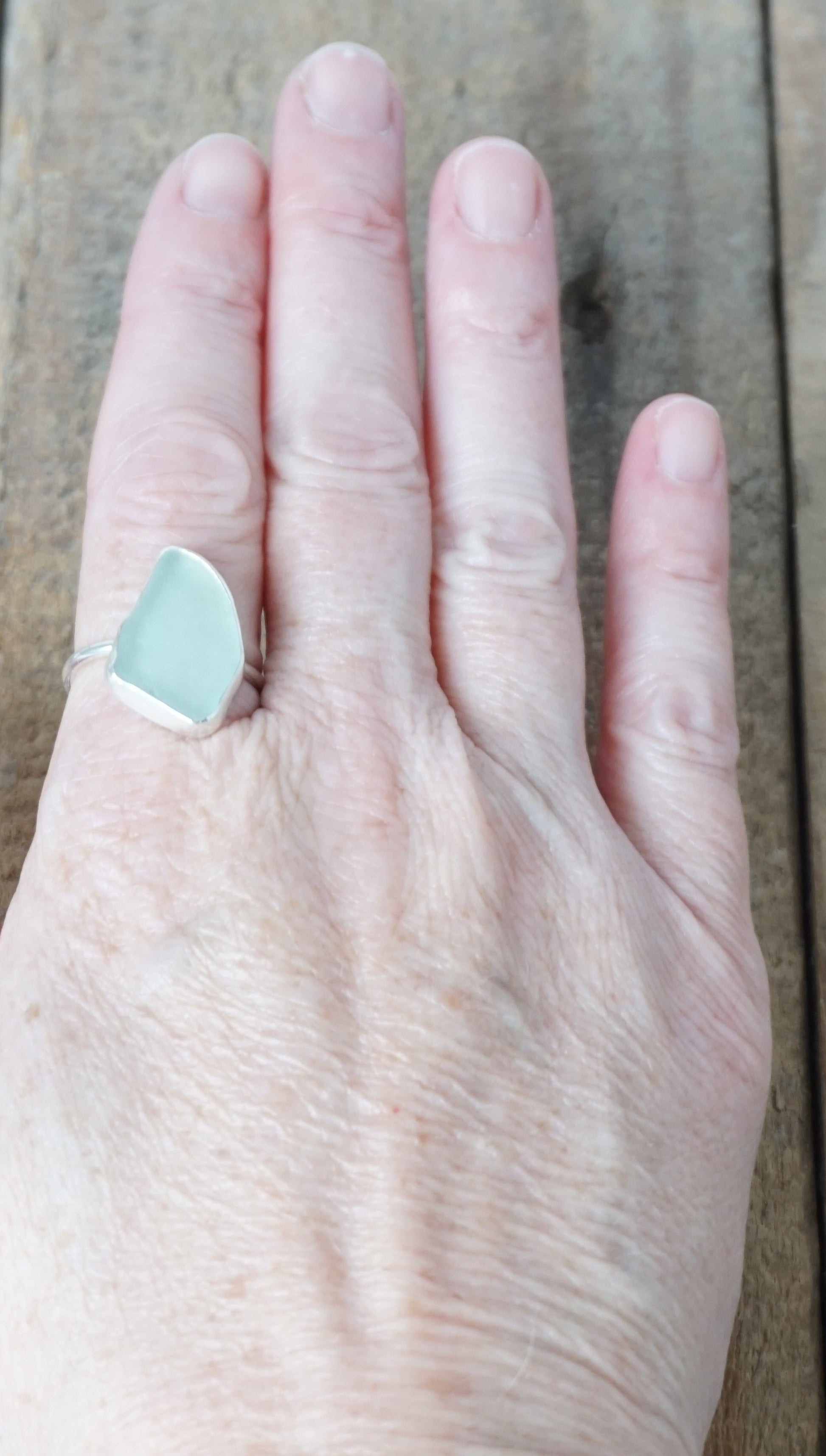 hand wearing a light aqua blue sea glass ring with a sterling silver setting, against a wooden background