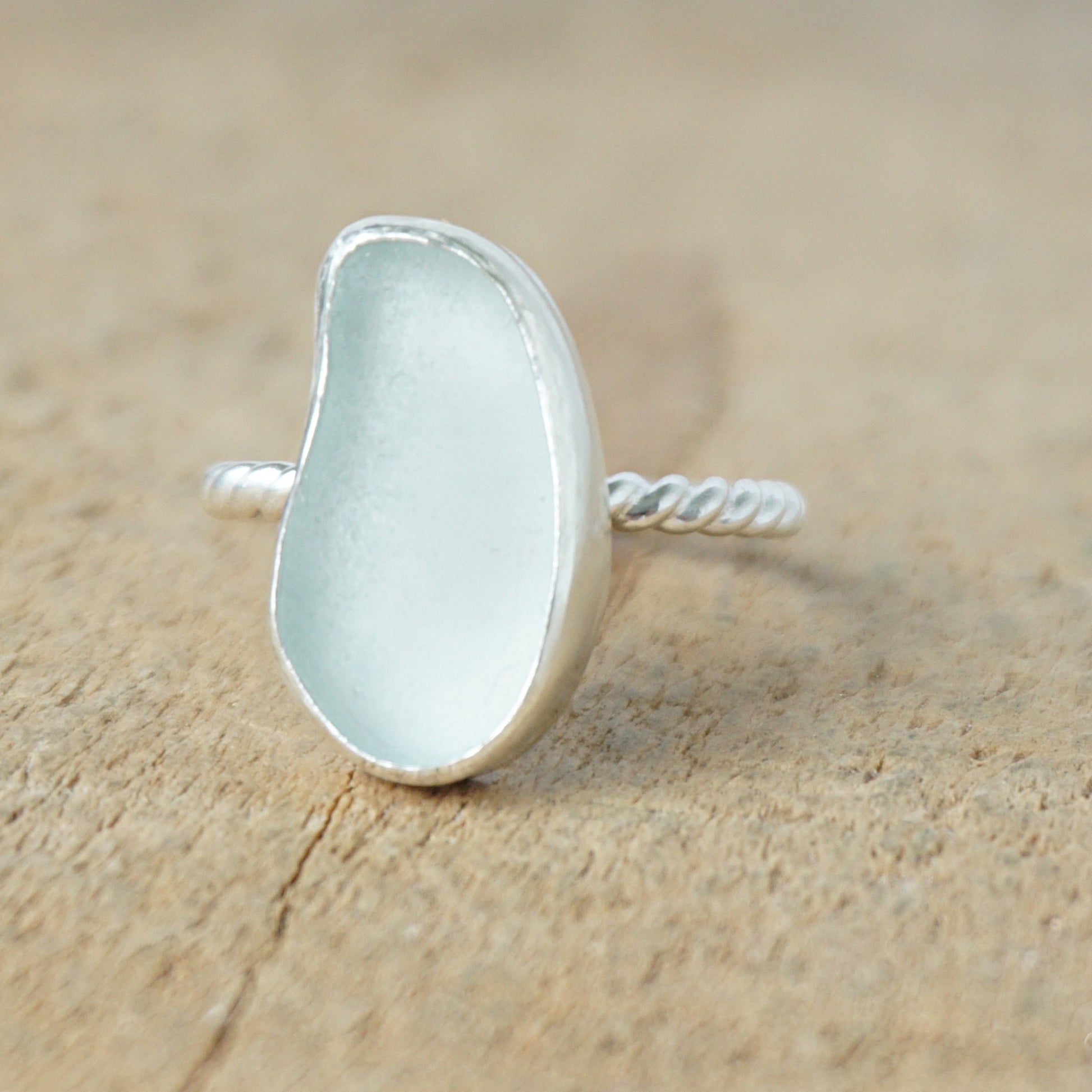 light aqua blue sea glass ring with a sterling silver setting, against a wooden background