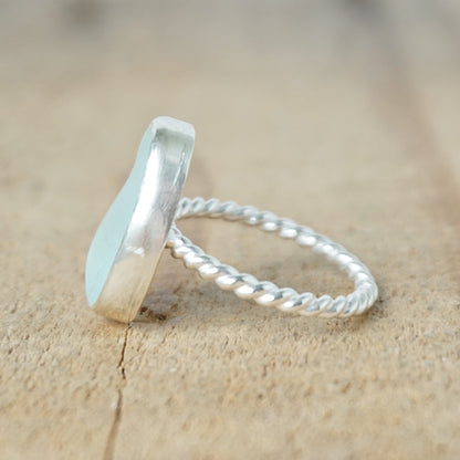 side view of a light aqua blue sea glass ring with a sterling silver setting, against a wooden background