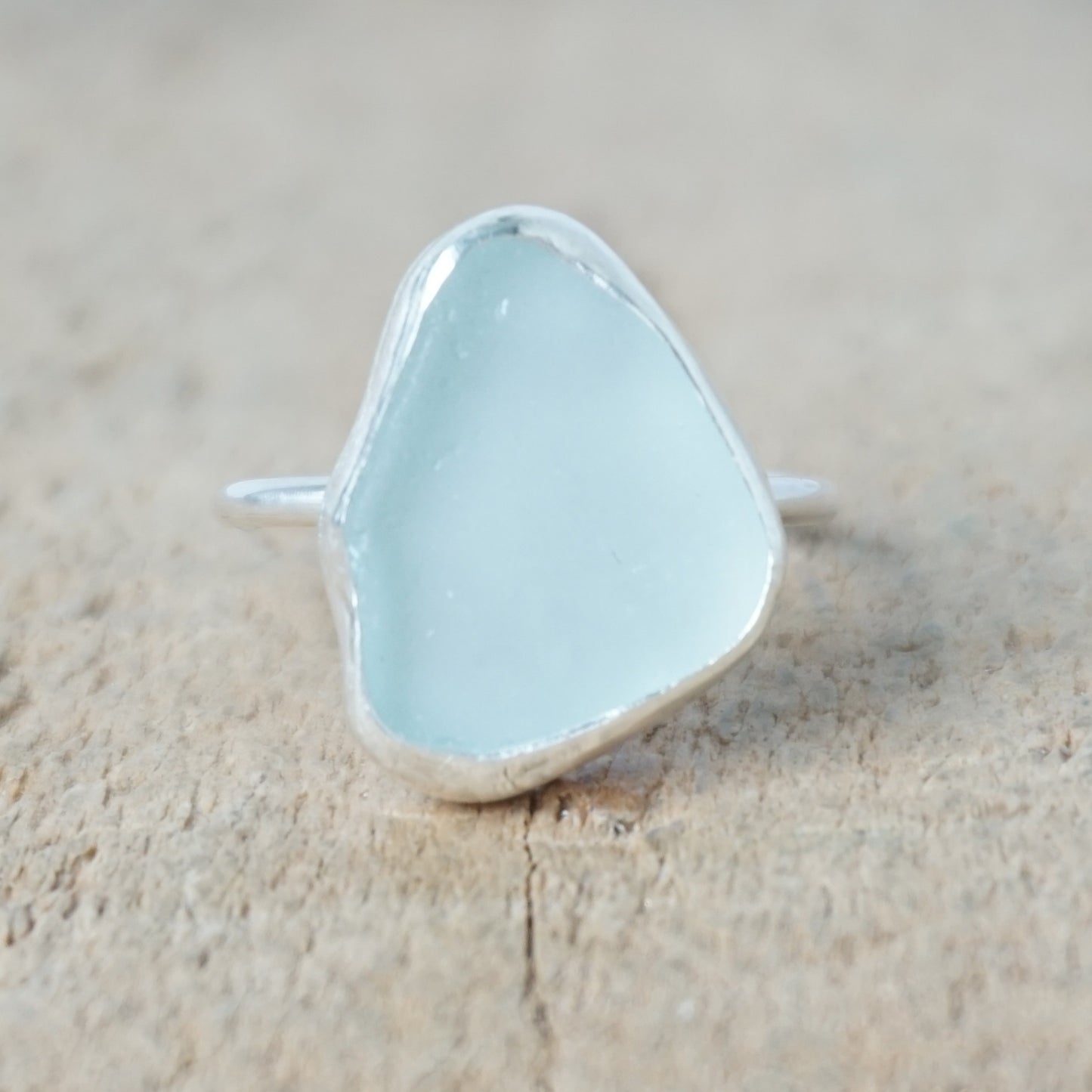 light aqua blue sea glass ring with a sterling silver setting, against a wooden background