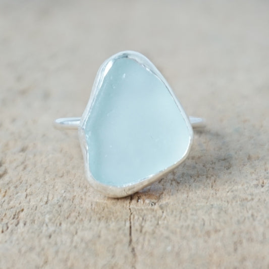 light aqua blue sea glass ring with a sterling silver setting, against a wooden background