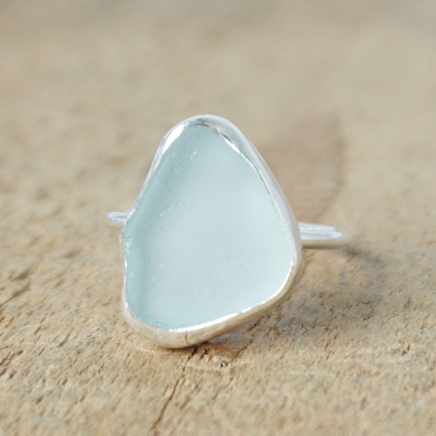 light aqua blue sea glass ring with a sterling silver setting, against a wooden background