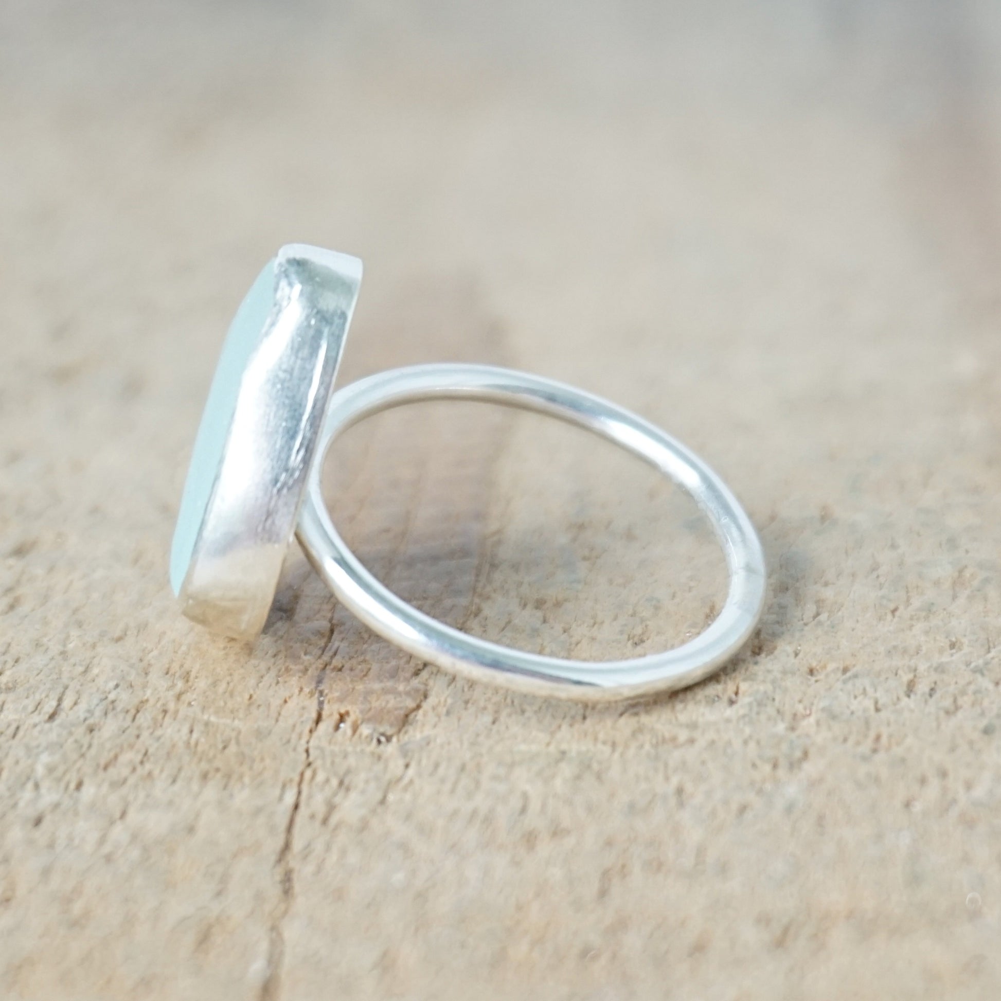 side view of a light aqua blue sea glass ring with a sterling silver setting, against a wooden background