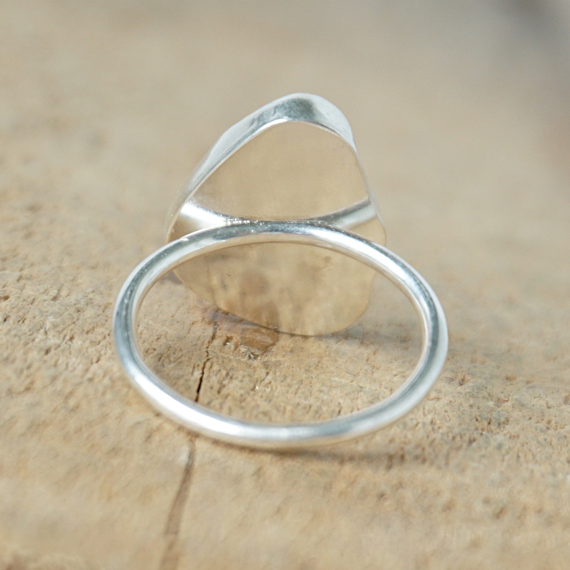 back view of a light aqua blue sea glass ring with a sterling silver setting, against a wooden background