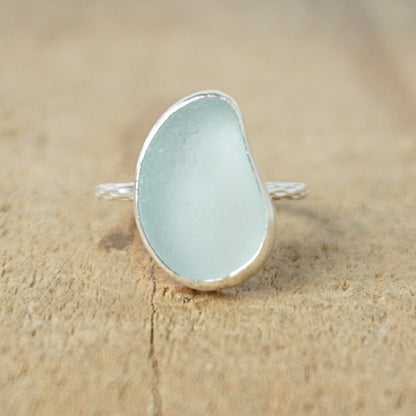 light aqua blue sea glass ring with a sterling silver setting, against a wooden background