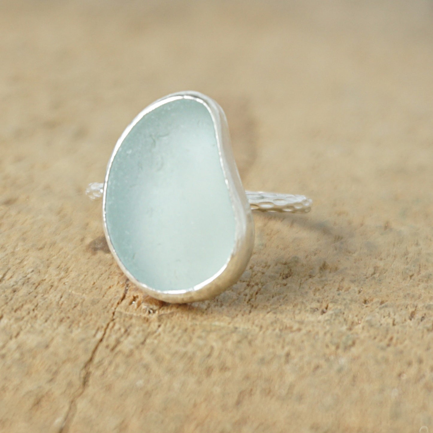 light aqua blue sea glass ring with a sterling silver setting, against a wooden background