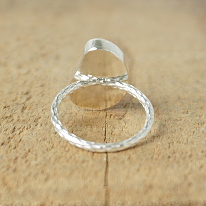 back view of a light aqua blue sea glass ring with a sterling silver setting, against a wooden background