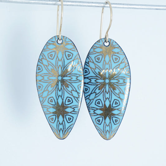 gold pattern on light blue enamel teardrop shaped earrings, on a white background