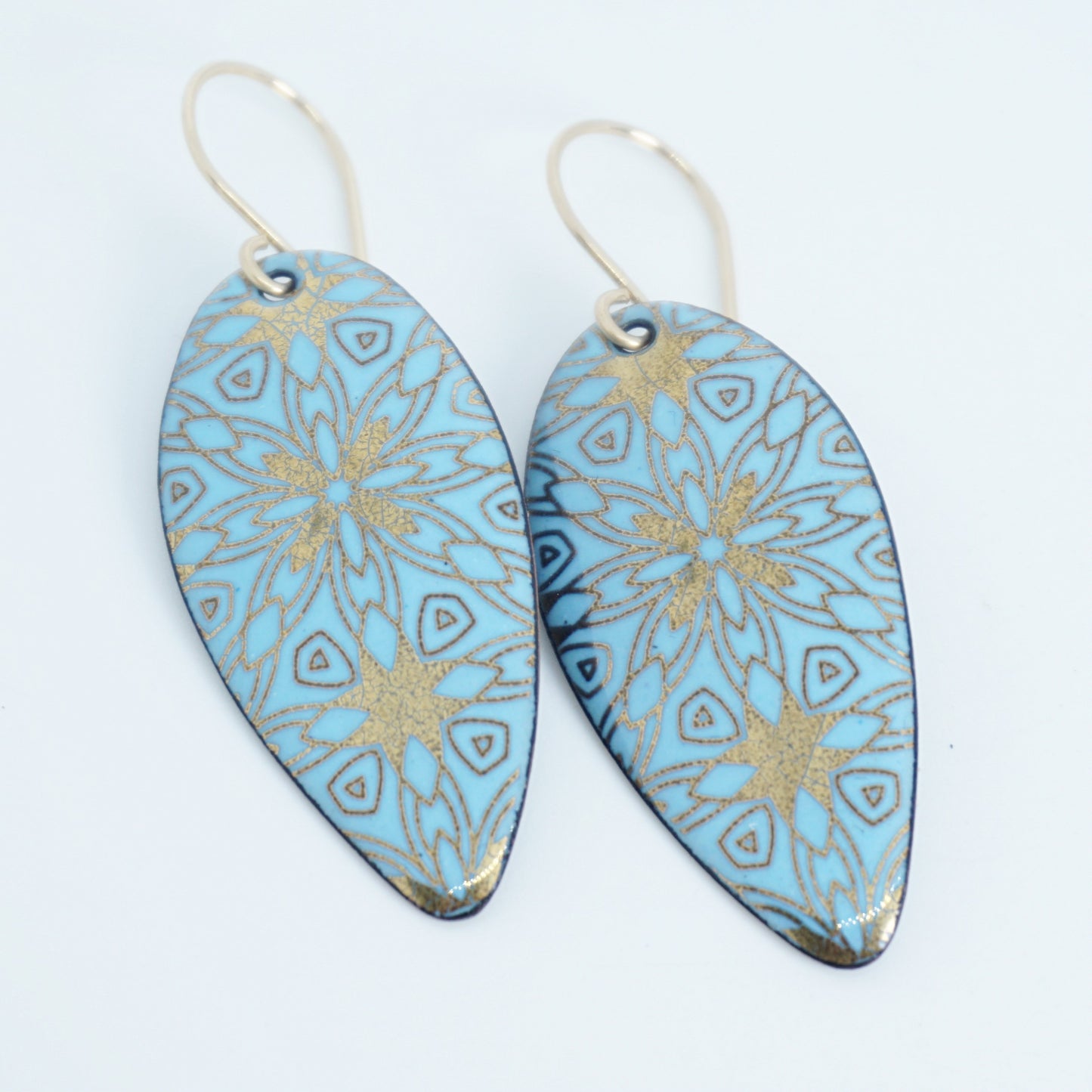gold pattern on light blue enamel teardrop shaped earrings, on a white background