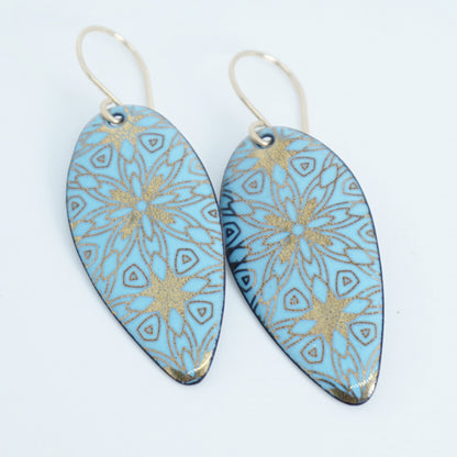 gold pattern on light blue enamel teardrop shaped earrings, on a white background