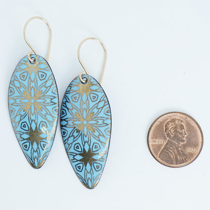 gold pattern on light blue enamel teardrop shaped earrings, next to a penny for scale, on a white background