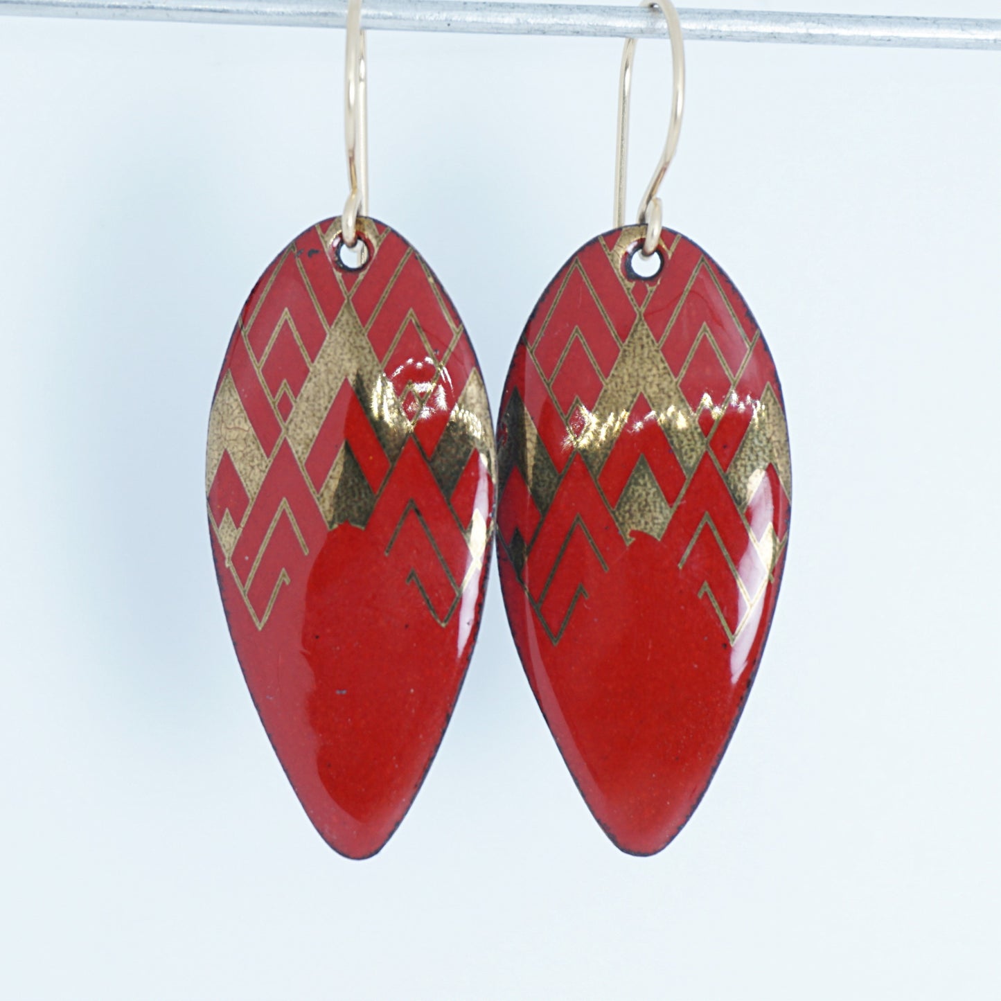 gold pattern on red enamel teardrop shaped earrings, on a white background