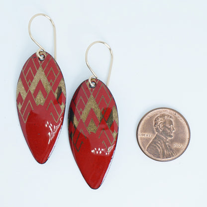 gold pattern on red enamel teardrop shaped earrings, next to a penny for scale, on a white background