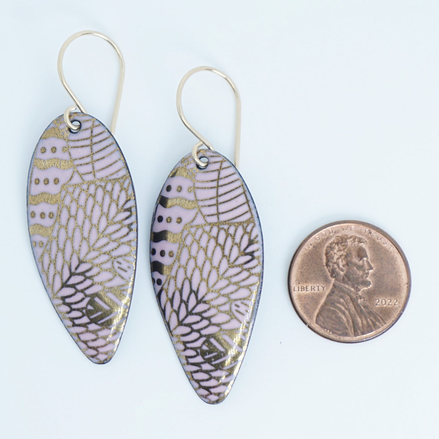 gold pattern on pink enamel teardrop shaped earrings, next to a penny for scale, on a white background