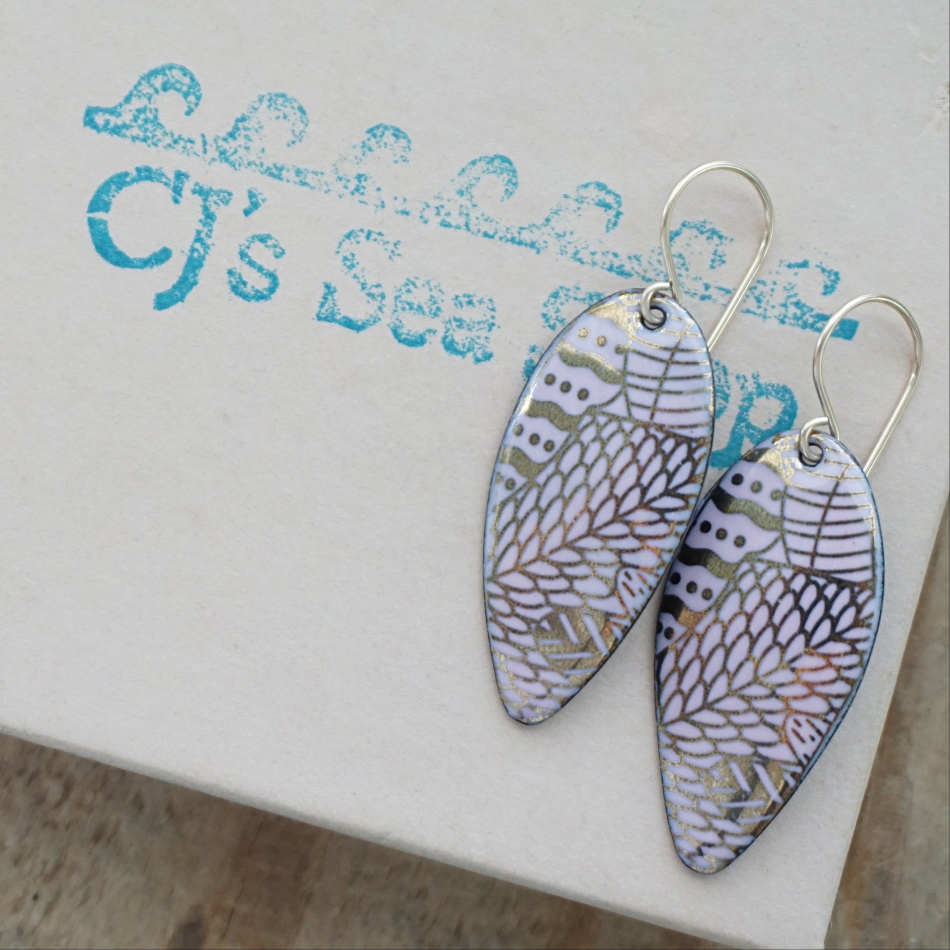 gold pattern on pink enamel teardrop shaped earrings, on a gift box