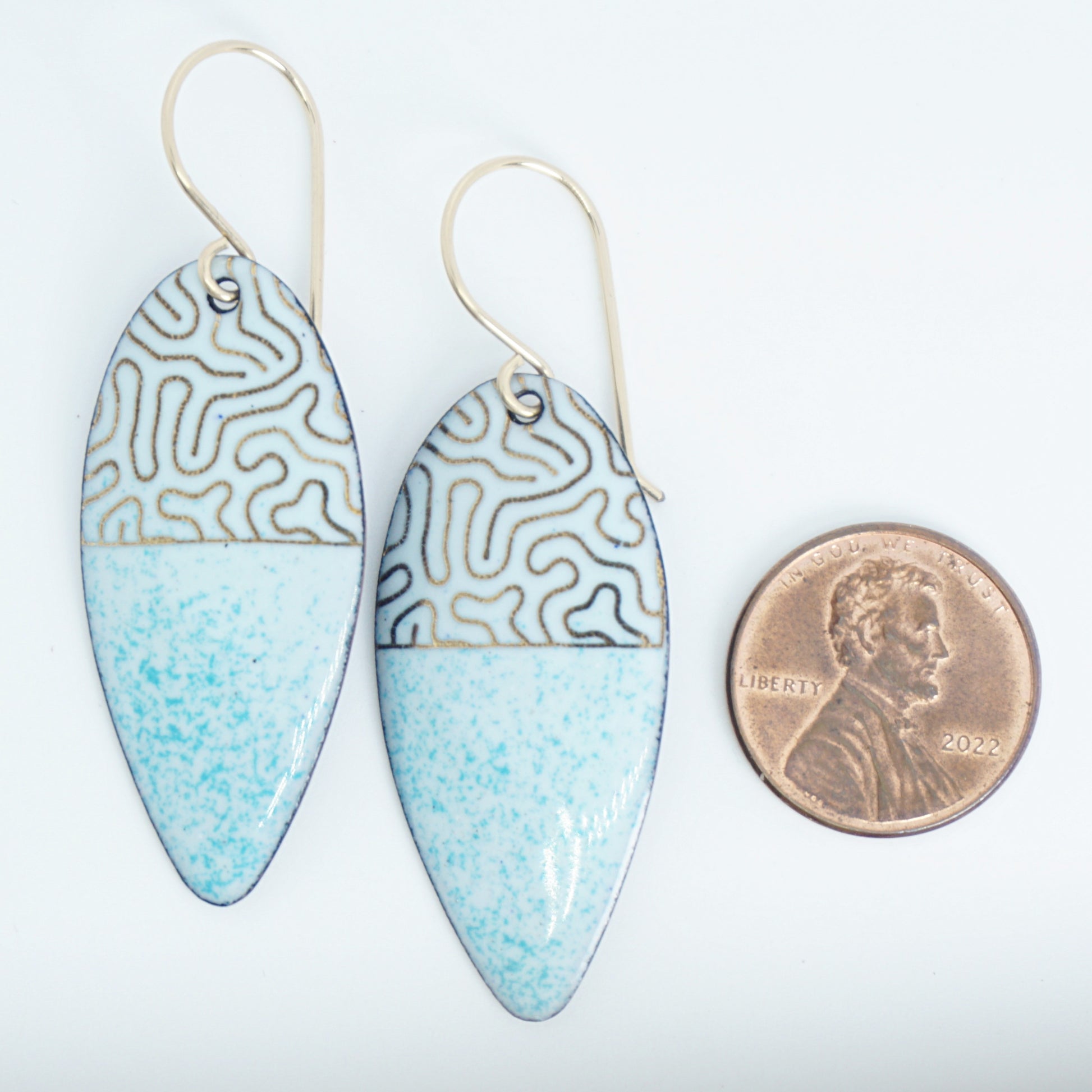 gold pattern on seafoam green enamel teardrop shaped earrings, next to a penny for scale, on a white background