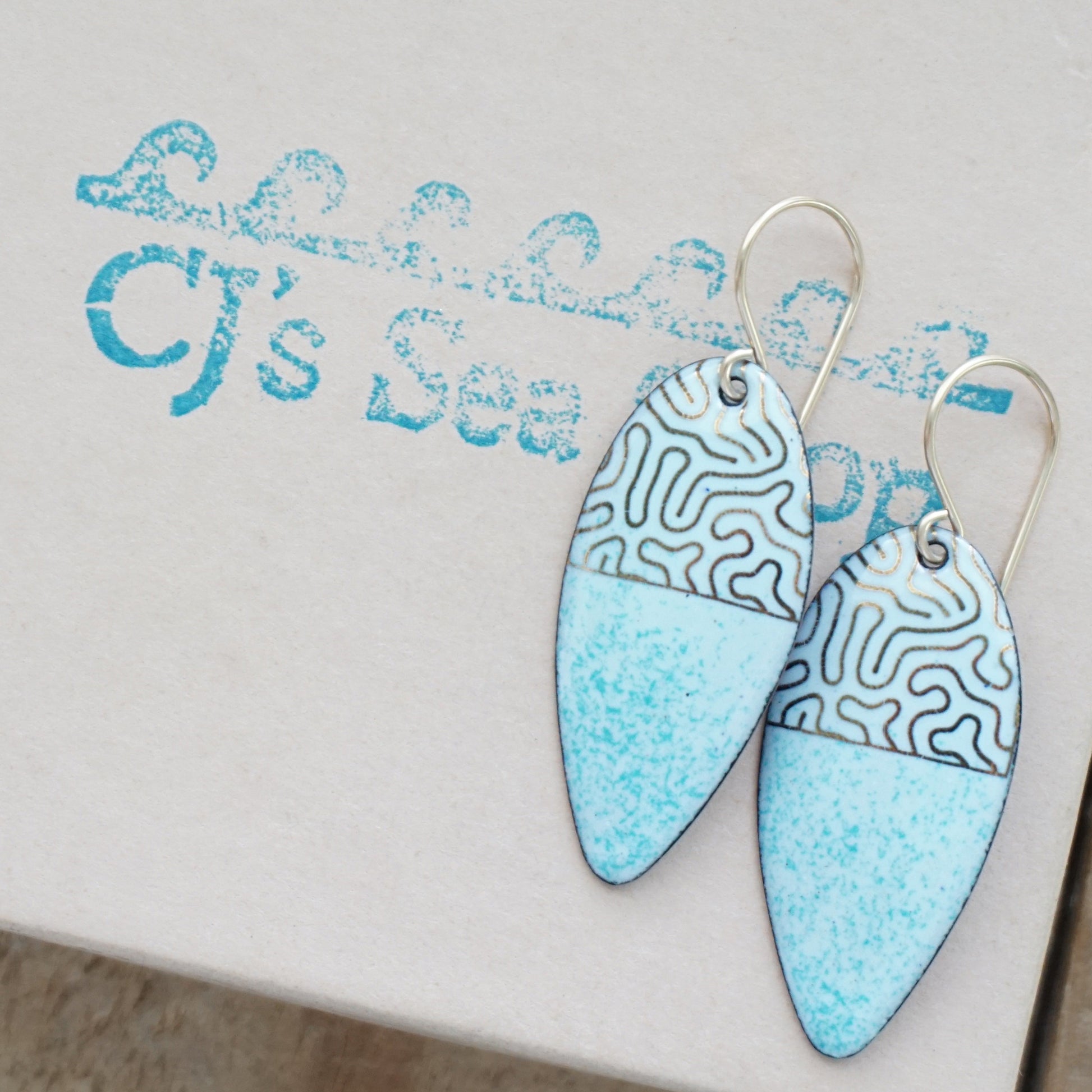 gold pattern on seafoam green enamel teardrop shaped earrings, on a gift box
