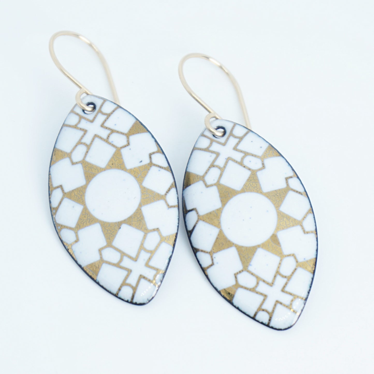 White, marquis shaped earrings with gold accents, against a white background