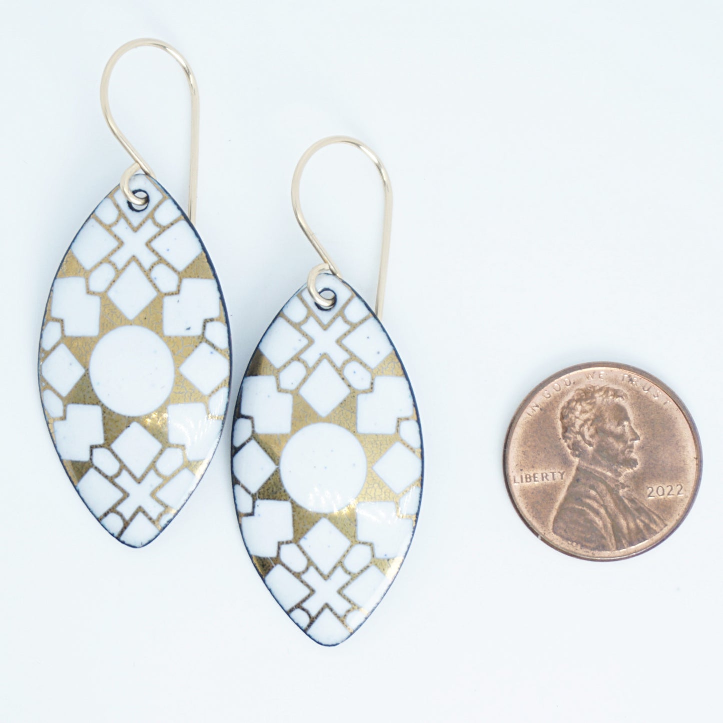 White, marquis shaped earrings with gold accents, next to a penny for scale, against a white background