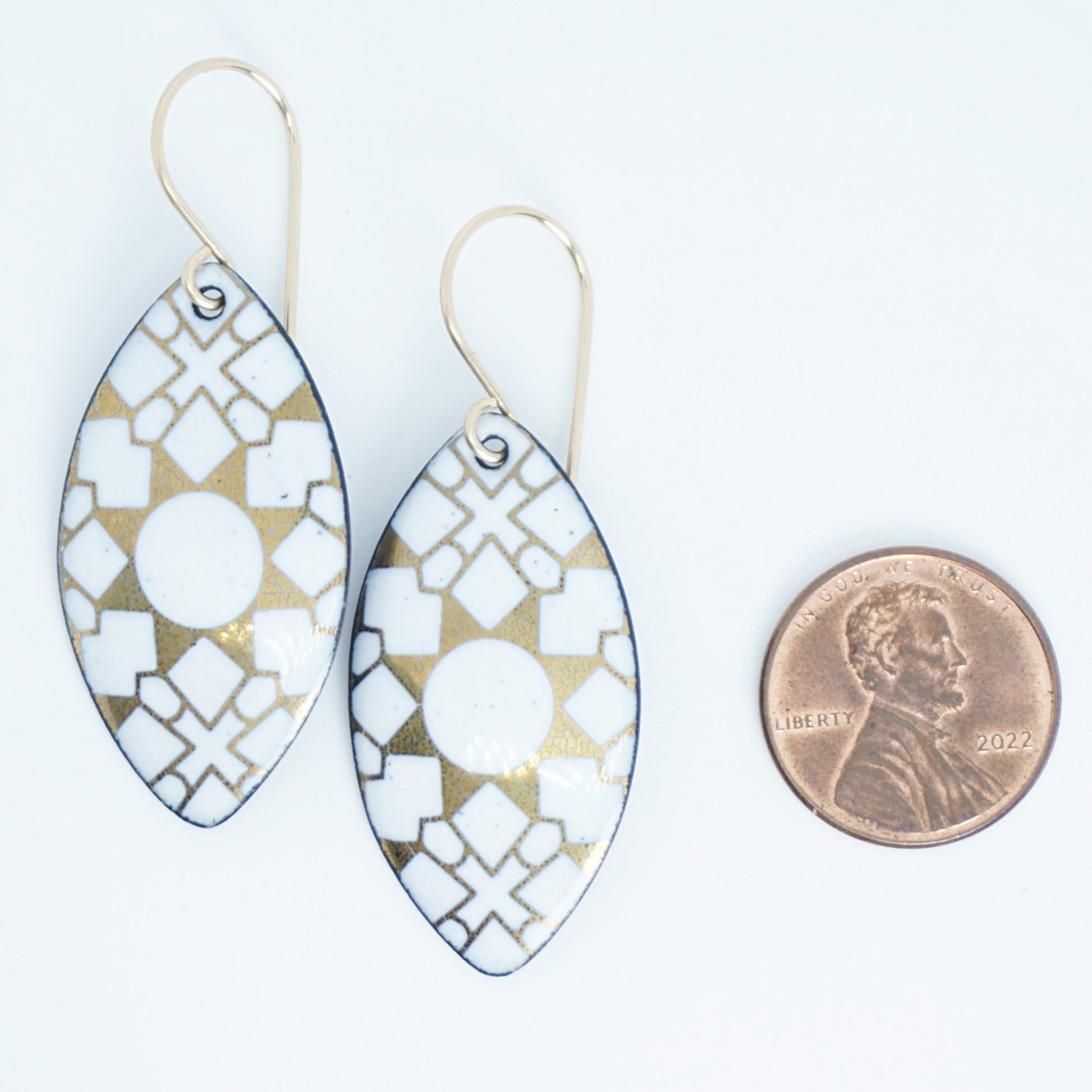White, marquis shaped earrings with gold accents, next to a penny for scale, against a white background