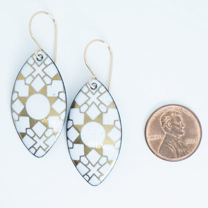 White, marquis shaped earrings with gold accents, next to a penny for scale, against a white background