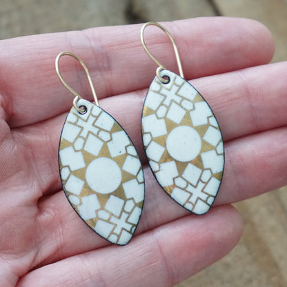 hand holding a pair of White, marquis shaped earrings with gold accents, against a wooden background