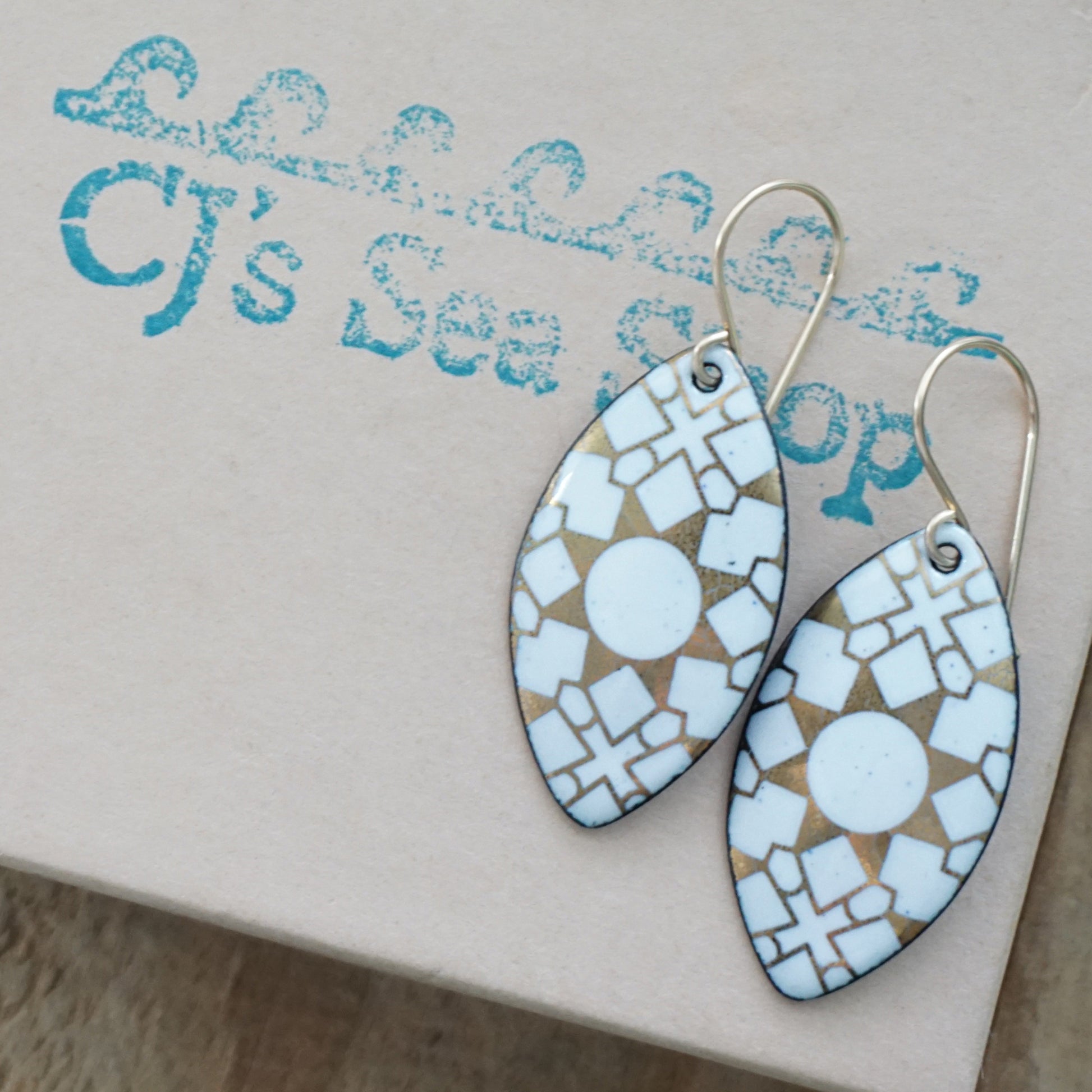 White, marquis shaped earrings with gold accents, on a gift box