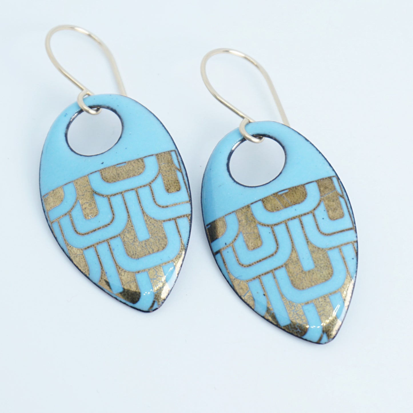 Light blue, teardrop shaped earrings with gold accents, against a white background