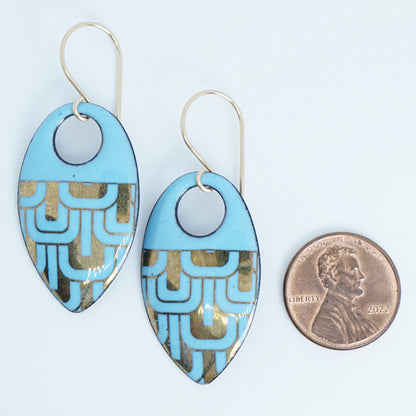 Light blue, teardrop shaped earrings with gold accents, next to a penny for scale, against a white background
