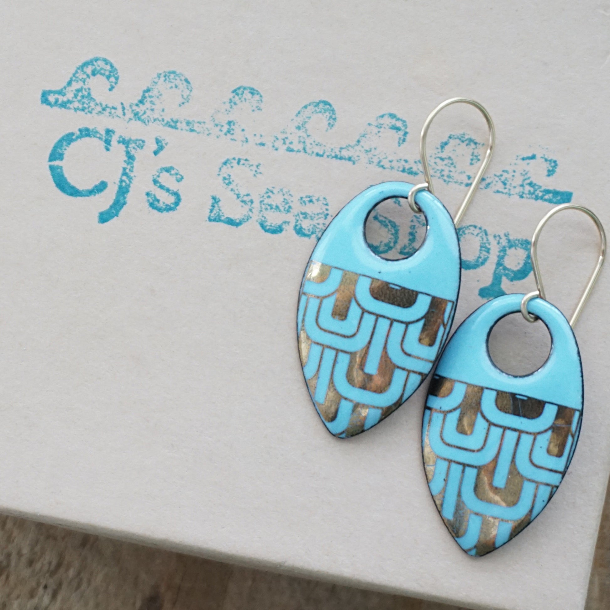 Light blue, teardrop shaped earrings with gold accents, on a gift box