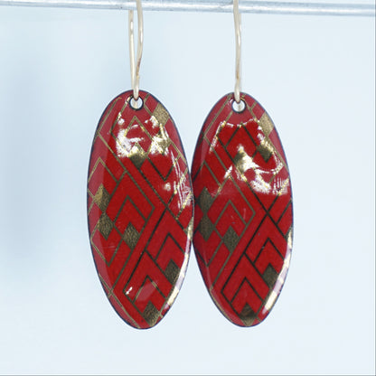 Red, oval shaped earrings with gold accents, against a white background