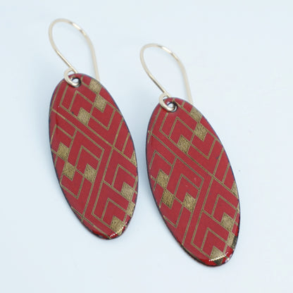 Red, oval shaped earrings with gold accents, against a white background