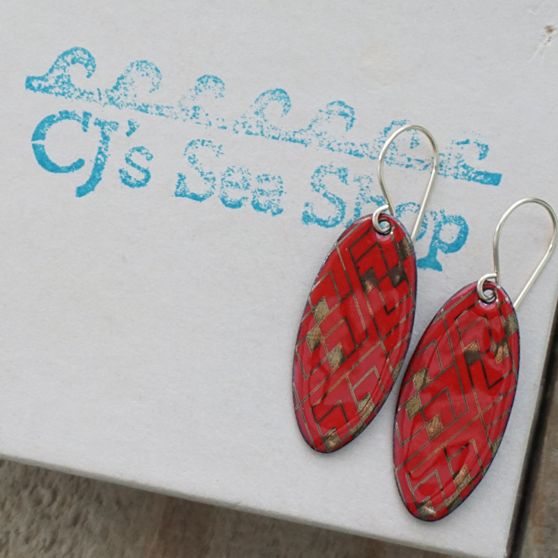 Red, oval shaped earrings with gold accents, on a gift box