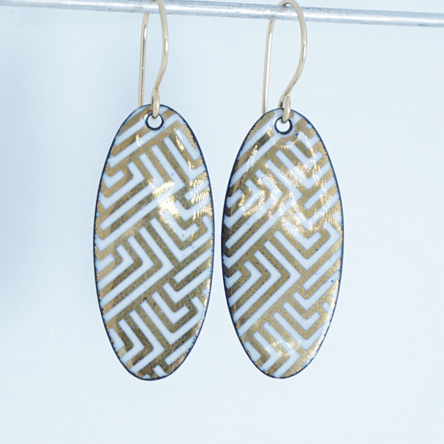 White, oval shaped earrings with gold accents, against a white background
