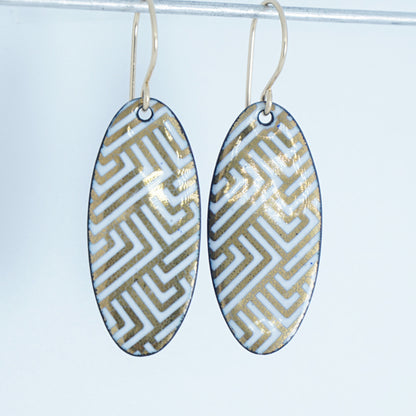 White, oval shaped earrings with gold accents, against a white background