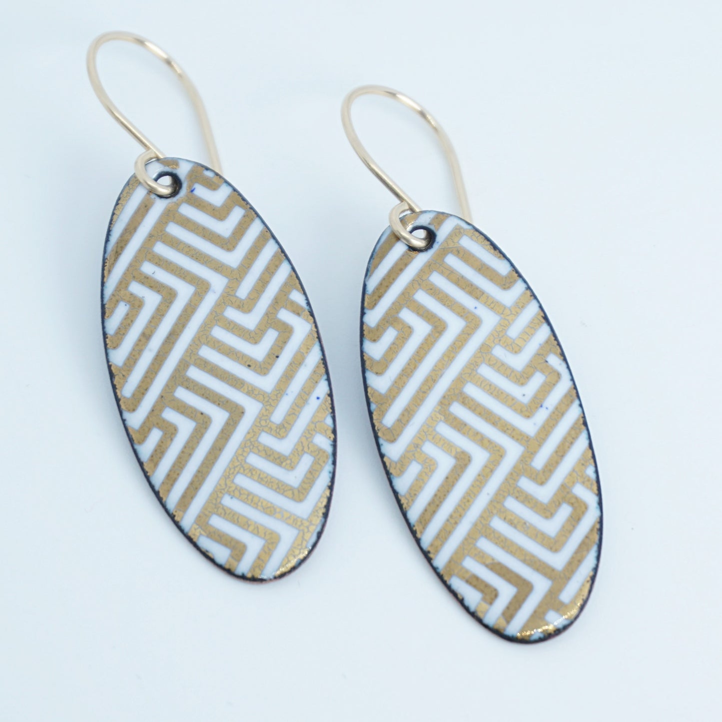 White, oval shaped earrings with gold accents, against a white background
