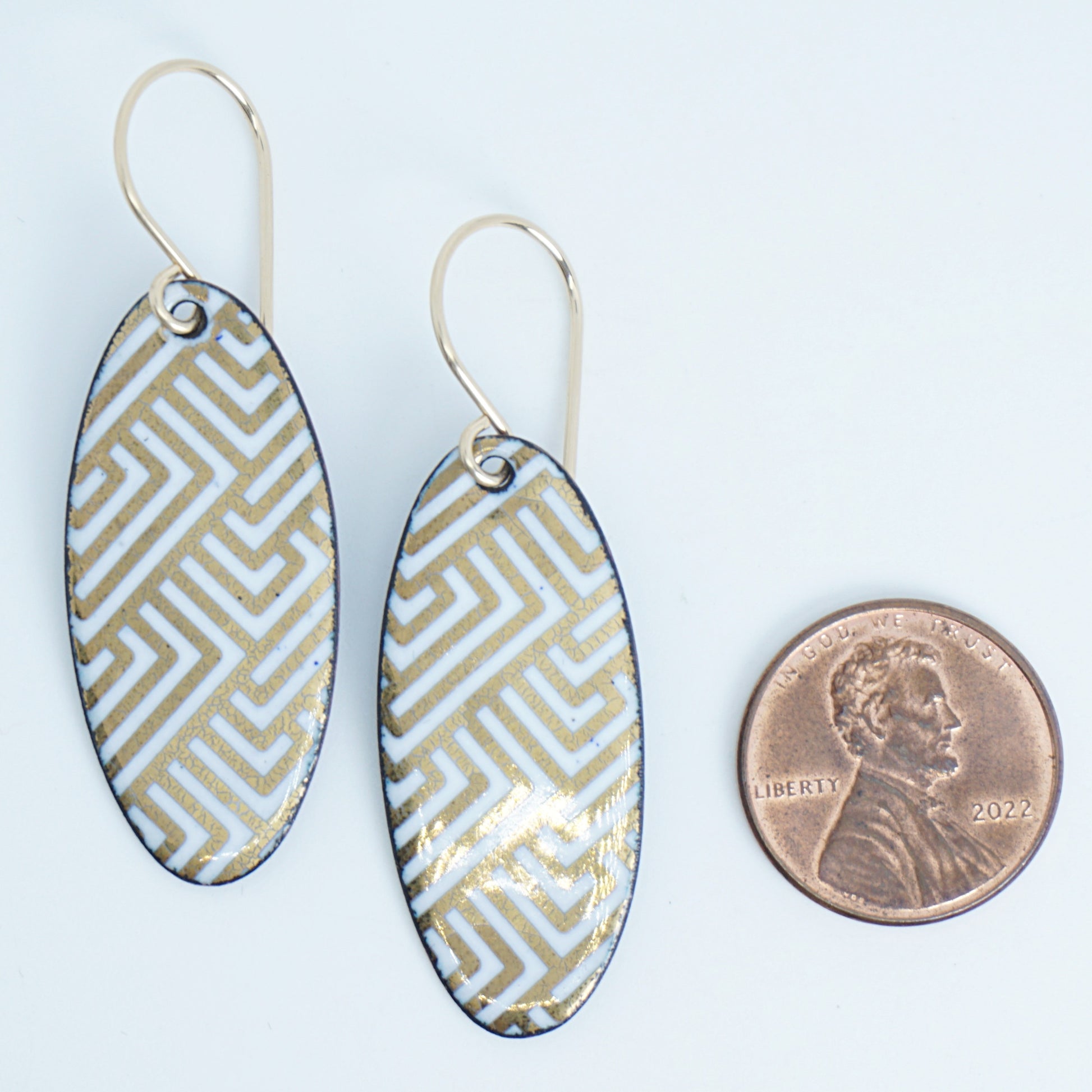 White, oval shaped earrings with gold accents, next to a penny for scale, against a white background