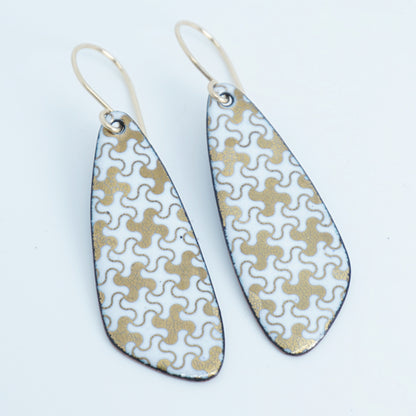 A pair of teardrop-shaped dangle earrings with a white and gold interlocking puzzle piece pattern, suspended from thin gold fishhook wires, shown on a plain white background.