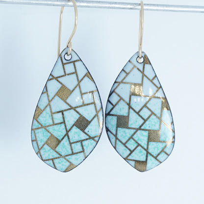 A pair of leaf-shaped dangling earrings with a mosaic pattern in light green, white, and metallic gold, suspended from thin gold hooks against a white background.