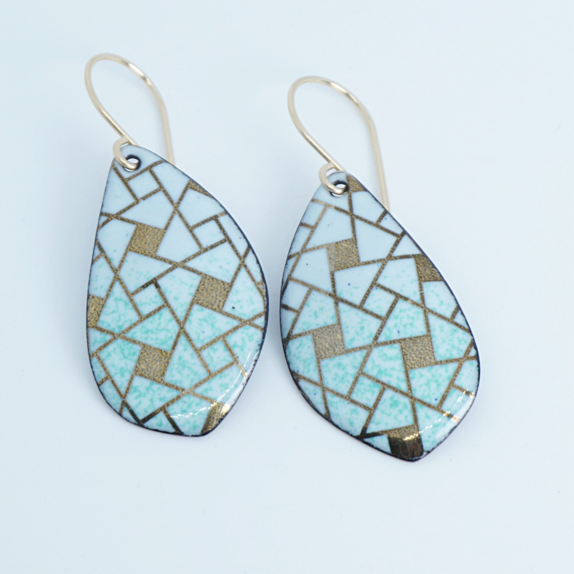 A pair of leaf-shaped drop earrings with a mosaic pattern of light green and gold tiles, suspended from gold fishhook wires on a white background