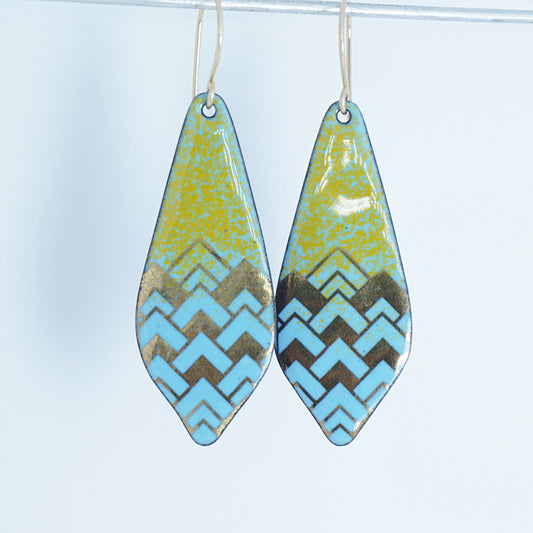 A pair of dangling teardrop-shaped earrings with a colorful geometric pattern. The top half of each earring is orange, and the bottom half features a chevron pattern in light blue and gold, against a white background