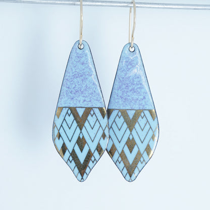 A pair of teardrop-shaped dangle earrings with a light blue and purple top half and a geometric chevron pattern in light blue and metallic gold on the bottom half, hanging from thin gold hooks against a plain light background.