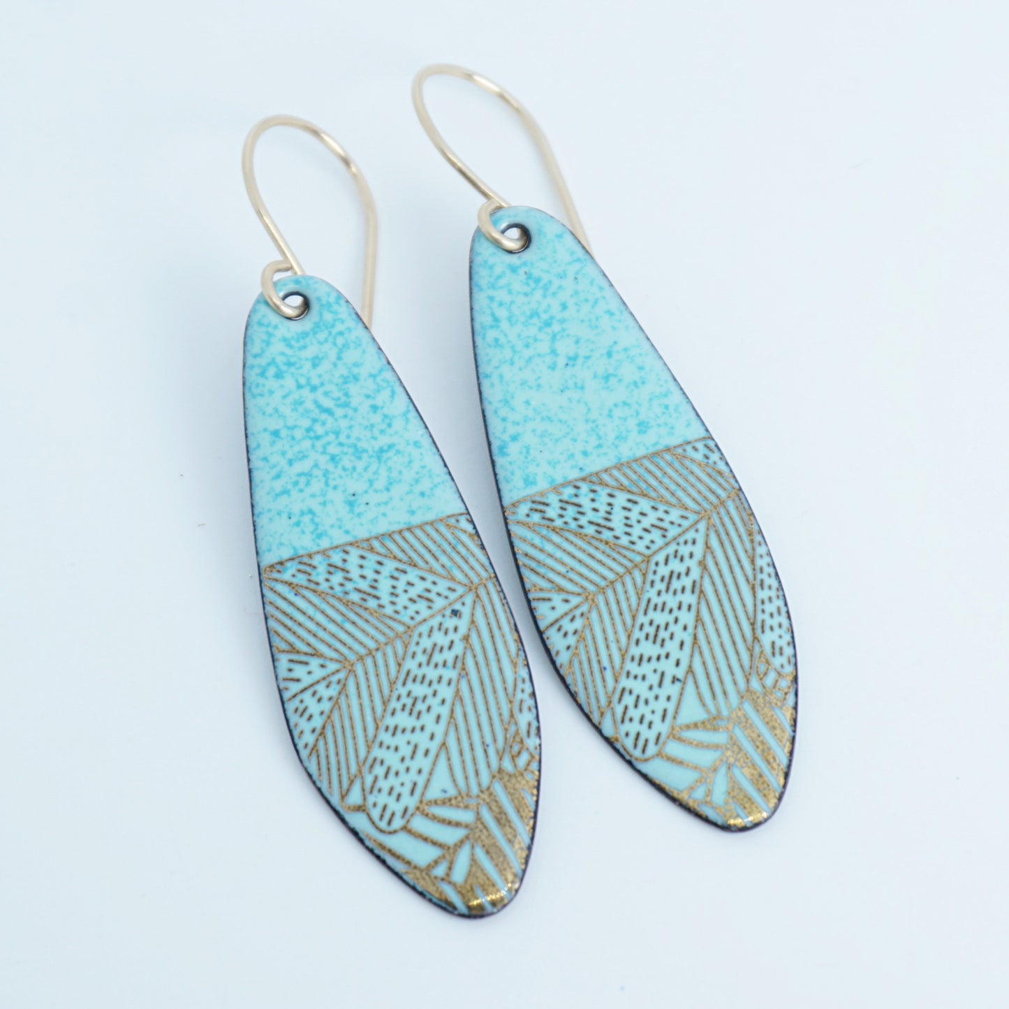 A pair of seafoam green teardrop shaped earrings with gold abstract accents, suspended from thin gold hooks on a white background