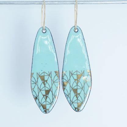 A pair of seafoam green teardrop shaped earrings with gold geometric accents, suspended from thin gold hooks on a white background