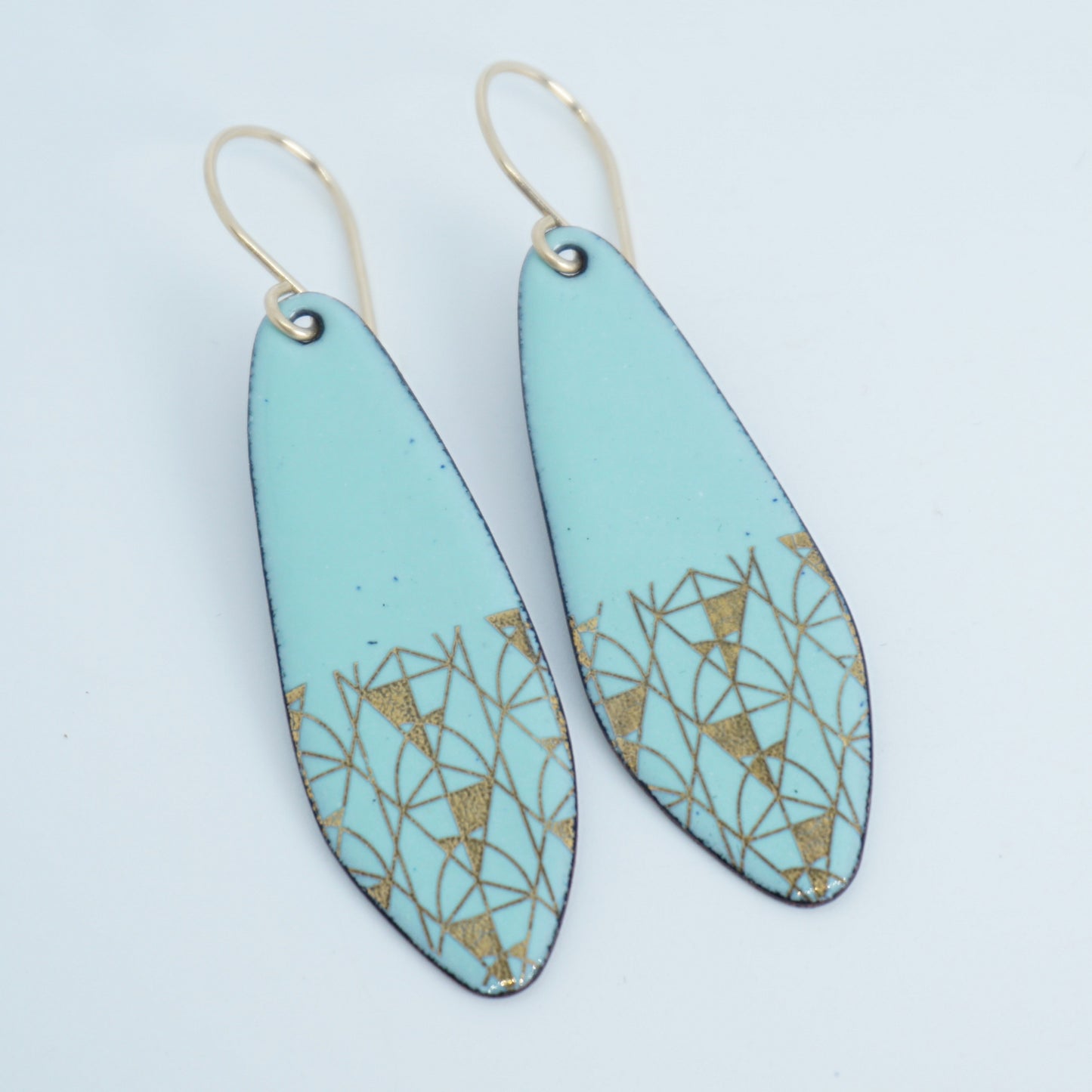 A pair of seafoam green teardrop shaped earrings with gold geometric accents, suspended from thin gold hooks on a white background