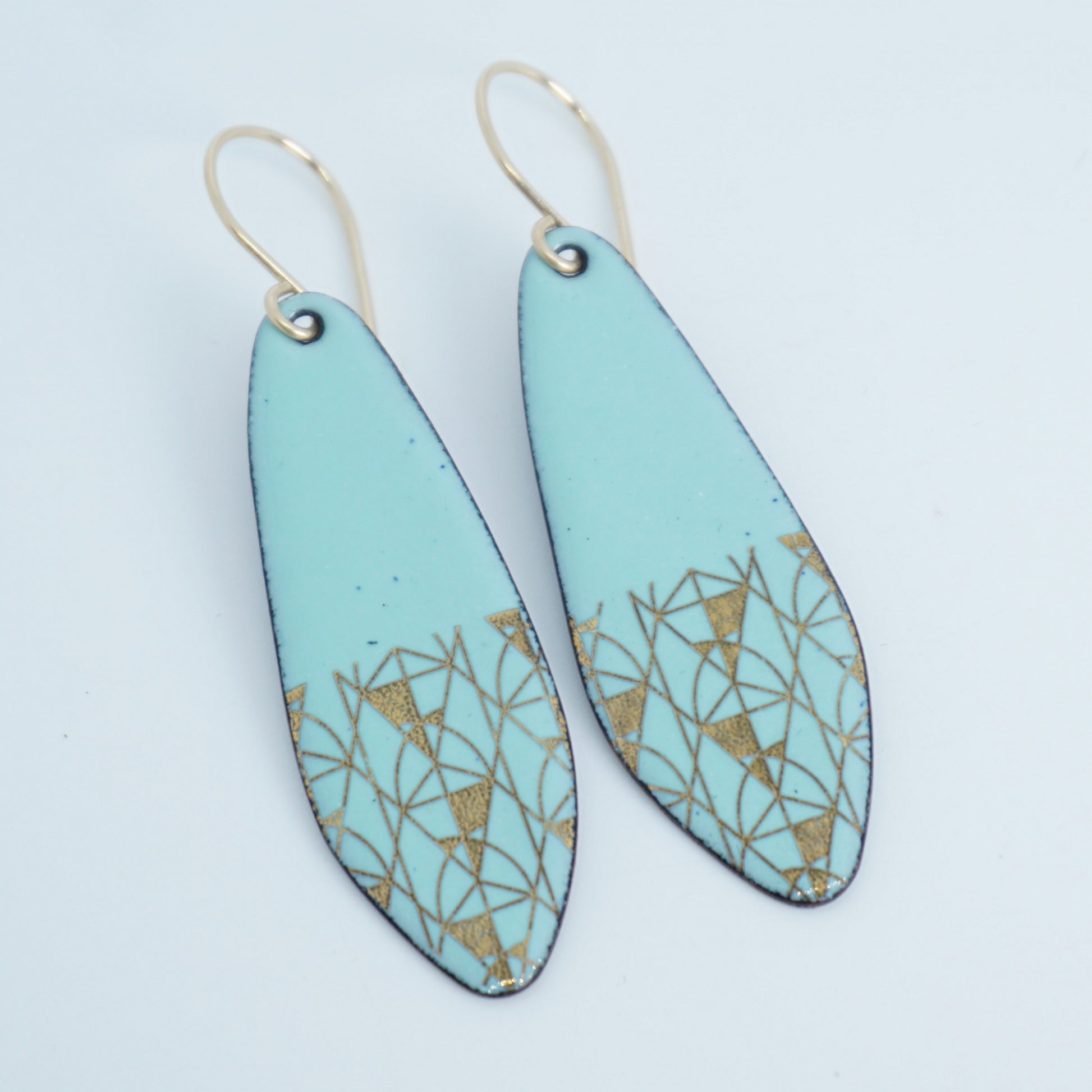 A pair of seafoam green teardrop shaped earrings with gold geometric accents, suspended from thin gold hooks on a white background